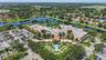 Aerial perspective of a large complex featuring a clay tile roof, central swimming pool, ornamental fountain, paved parking area, and mature palm land