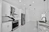 Kitchen featuring white shaker-style cabinetry, a contrasting patterned stone backsplash and waterfall island countertop, stainless steel appliances, 