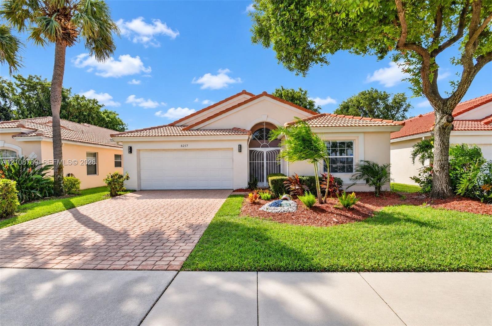 Single-story residence featuring a tile roof, brick-paver driveway, double-car garage, and an arched entryway with decorative metal security door