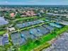 Community recreational area featuring multiple fenced tennis courts with shaded seating, paved parking area, and manicured green space along the water