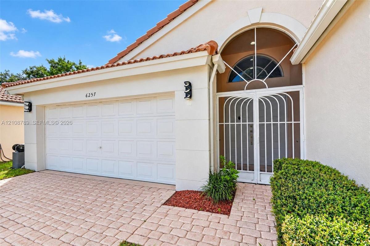 Stucco exterior featuring a dual-car garage, arched entryway with decorative metal screening, semi-circular transom window, and stone-paver driveway