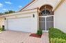 Stucco exterior featuring a dual-car garage, arched entryway with decorative metal screening, semi-circular transom window, and stone-paver driveway