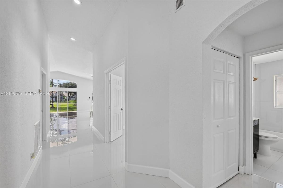 Hallway featuring polished light-toned floor tile, recessed ceiling lighting, arched wall detailing, and dual-panel interior doors