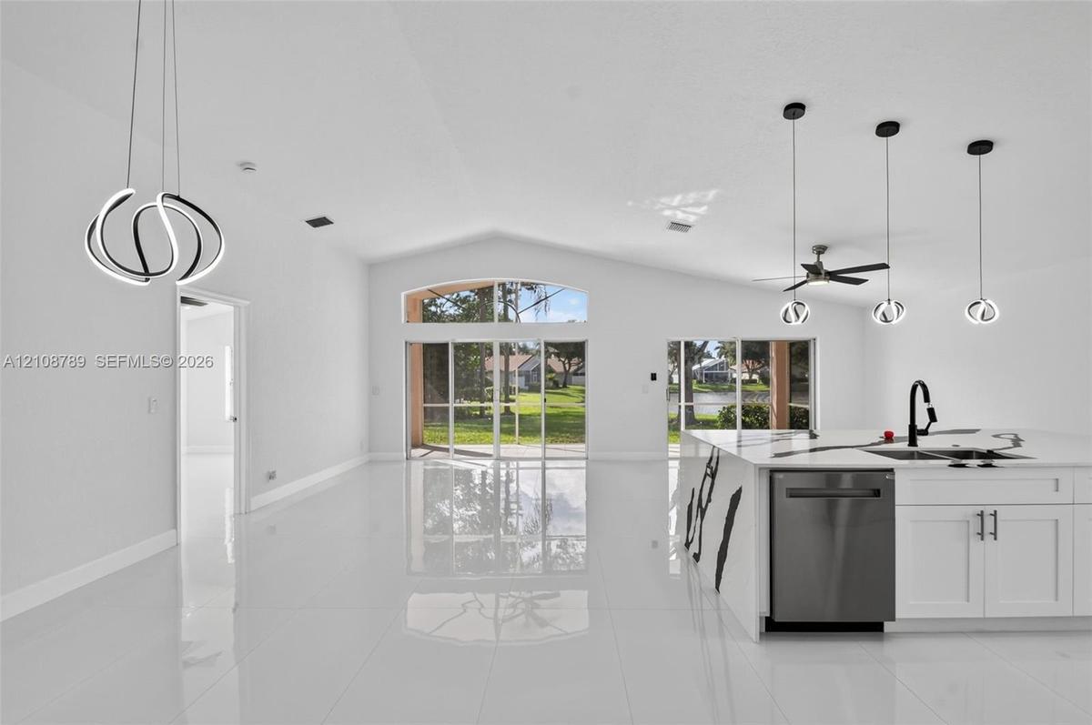 Open-concept interior featuring vaulted ceilings, polished tile flooring, a large kitchen island with waterfall-edge stone countertop, contemporary LE