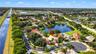 Aerial perspective of a single-story residence featuring a tile roof, paved driveway, and direct frontage on a pond