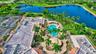 Aerial perspective of the property featuring a swimming pool, covered outdoor pavilion, paver patio, mature palm trees, and water frontage