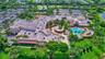 Aerial view of a sprawling commercial complex featuring a terracotta-tiled roof, an outdoor swimming pool, integrated landscaping with mature palm tre