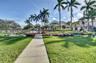Landscaped grounds featuring a paved walkway, manicured lawn, established palm trees, and floral garden beds