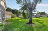 Expansive backyard featuring a large grass lawn, mature trees, white vinyl privacy fencing, and a screened-in structural enclosure