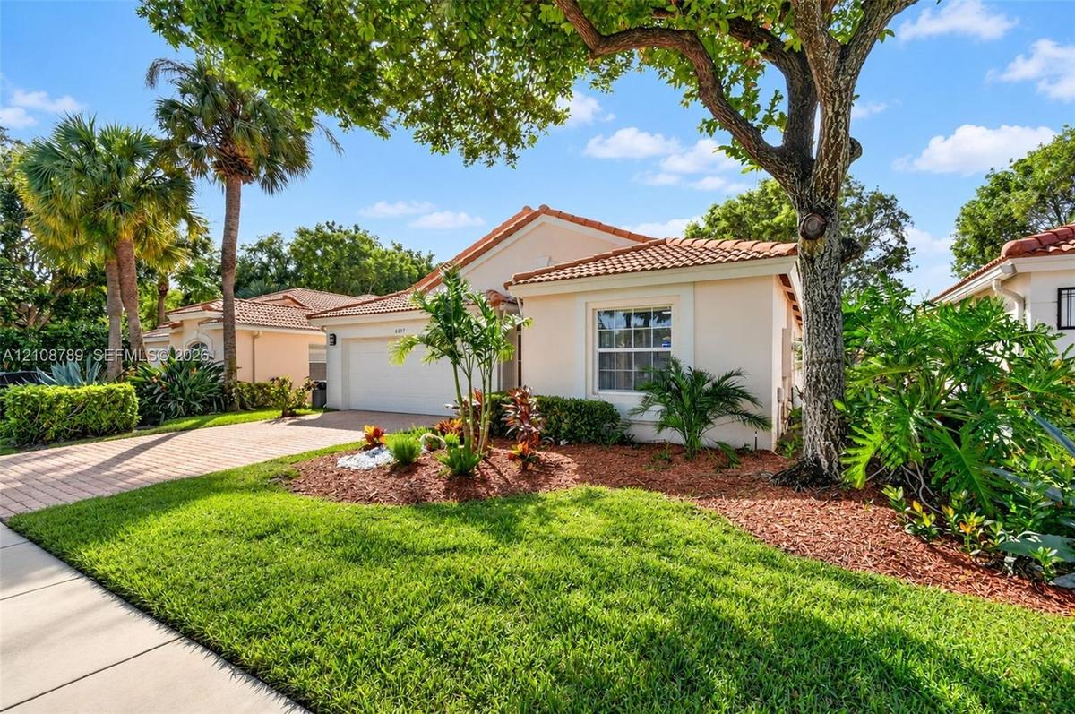 Single-story residence featuring a tile roof, light-toned stucco exterior, attached garage, paver driveway, and mature landscaping