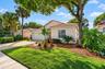 Single-story residence featuring a tile roof, light-toned stucco exterior, attached garage, paver driveway, and mature landscaping