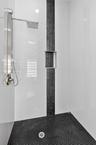 Shower featuring large-format white wall tile, a vertical decorative stone accent strip, a built-in recessed niche, stainless steel rainfall shower pa