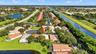 Aerial perspective of a property situated in a cul-de-sac featuring mature landscaping, tile roofing, and expansive grounds bordering a waterway