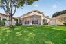 Exterior featuring a screened-in lanai, tile roof, and vinyl privacy fencing surrounding a lawn with mature trees