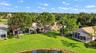 Expansive rear yard featuring a manicured lawn, perimeter water frontage, mature shade trees, and screened-in lanais