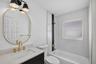 Bathroom featuring a vanity with a light-toned countertop, an oval mirror with a gold-finish frame, brass-tone hardware, a three-light fixture, and a 