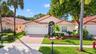 Stucco exterior featuring a terracotta-style tile roof, paver driveway, arched entryway with a decorative security gate, and mature palm trees