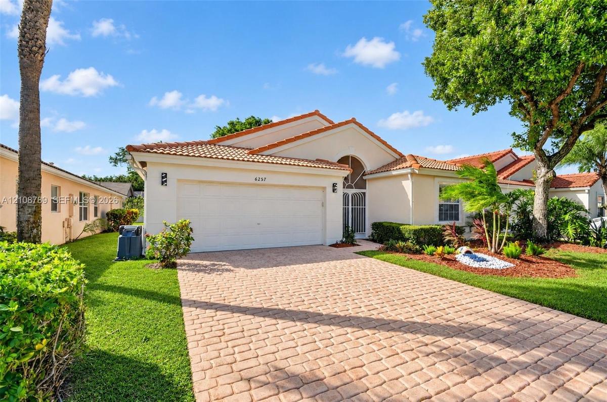 Single-story residence featuring a terracotta-tile roof, paved driveway, two-car garage, stucco exterior, and arched entryway with decorative metal sc