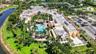 Aerial perspective featuring a swimming pool, multiple palm trees, water frontage, and paved parking area