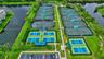 Tennis complex featuring multiple hard courts, fenced pickleball courts with overhead shading structures, landscaped grounds, and paved walkways
