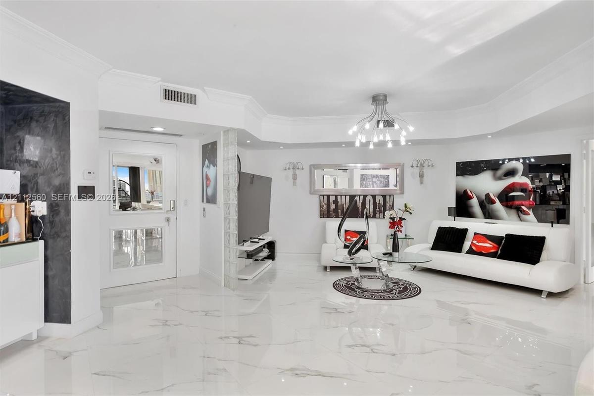Open living space featuring high-gloss large-format flooring, custom multi-arm chandelier, decorative glass block wall accent, and recessed ceiling li