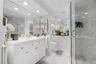 White vanity with an integrated countertop, full-width wall mirror, recessed ceiling lighting, and a glass-enclosed shower featuring large-format vein