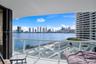 Private balcony featuring a glass-panel railing and tile flooring, oriented toward a water and city skyline backdrop