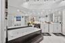 Jetted soaking tub with black tile surround, double vanity with white cabinetry, expansive wall-to-wall mirrors, recessed lighting, and large-format f