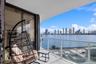 Covered balcony featuring white railings, tiled flooring, and sliding glass door access, highlighting water and city skyline scenery