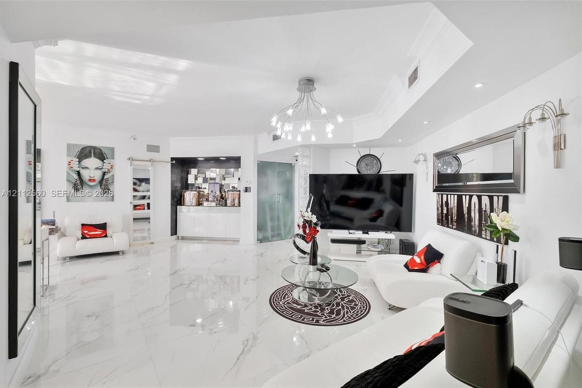 Large-format polished flooring, recessed ceiling lighting, multi-arm chandelier, built-in wet bar with high-gloss cabinetry, and frosted glass door