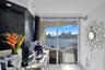 Floor-to-ceiling glass sliding doors opening to a balcony with water and skyline scenery, featuring a textured black feature wall, recessed lighting, 