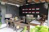 Covered outdoor kitchen featuring a multi-burner stainless steel grill, sleek cabinetry, integrated sink, and dark wood-finish paneled wall with decor