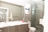 Dual-sink vanity with a white countertop and wood-finish cabinetry, frameless glass shower enclosure, and grey wood-finish tile shower wall