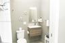 Floating vanity with wood-finish cabinetry, solid-surface countertop, rectangular mirror with integrated lighting, glass shelving, and standard flush 