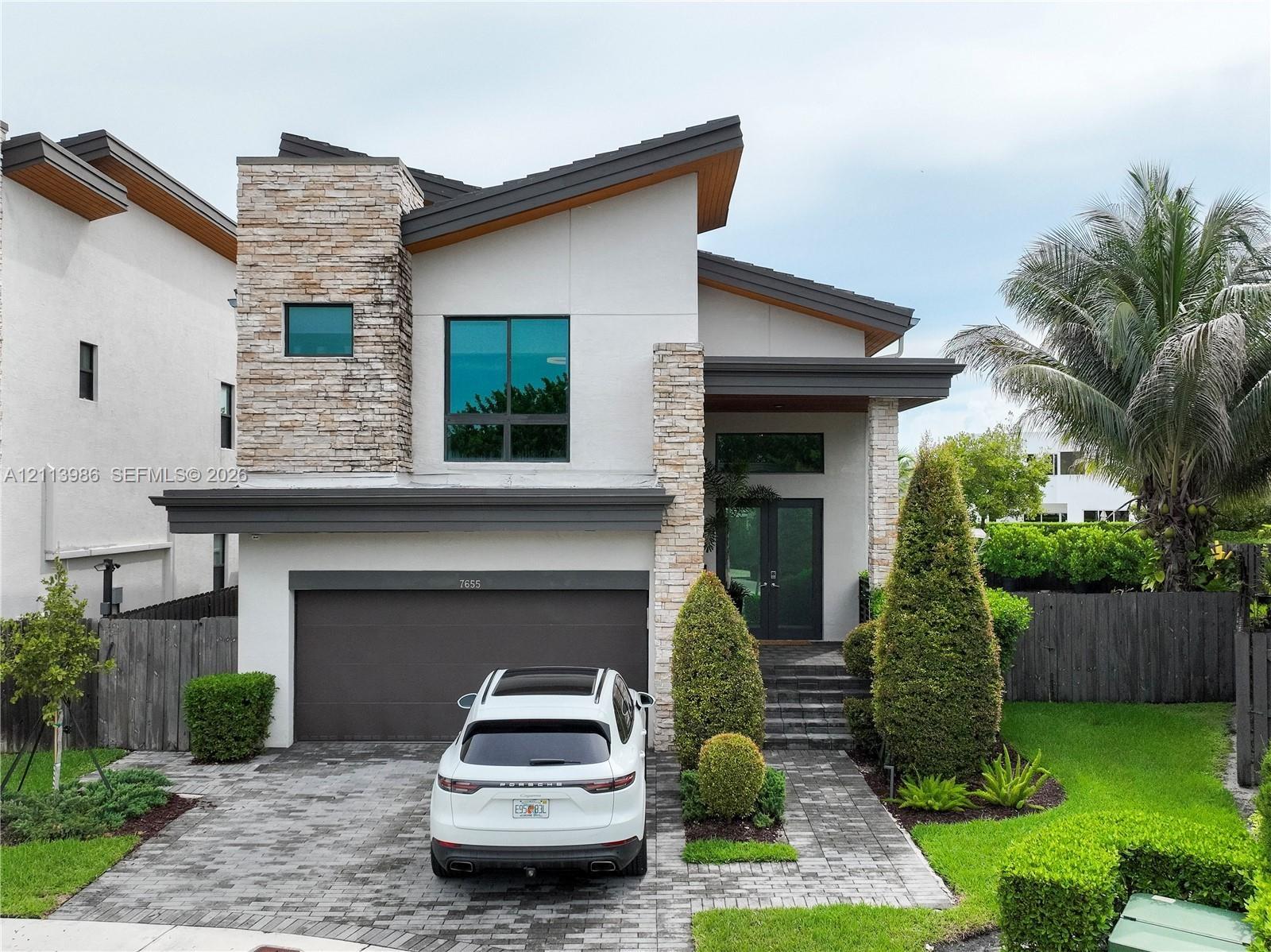 Modern exterior featuring stacked stone accents, smooth stucco finish, multi-level roofline, double-door entry, and a paver driveway