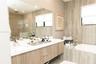 Floating wood-finish vanity with dual integrated sinks and polished chrome fixtures, oversized wall-to-wall mirror, built-in soaking tub, and tile-wra