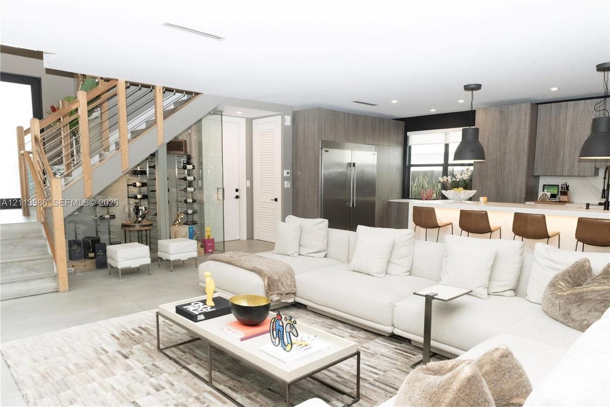 Open-concept kitchen featuring flat-panel cabinetry and stainless steel appliances, glass-enclosed wine storage, and a cable-railing staircase with wo