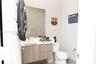 Modern vanity featuring light wood-finish cabinetry, a crisp white countertop, large wall-mounted mirror, and sleek metal hardware