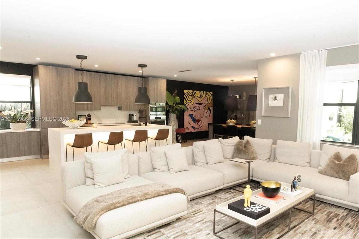 Open-concept interior featuring light wood-finish cabinetry, a large kitchen island with integrated under-counter lighting, stone slab surfacing, and 