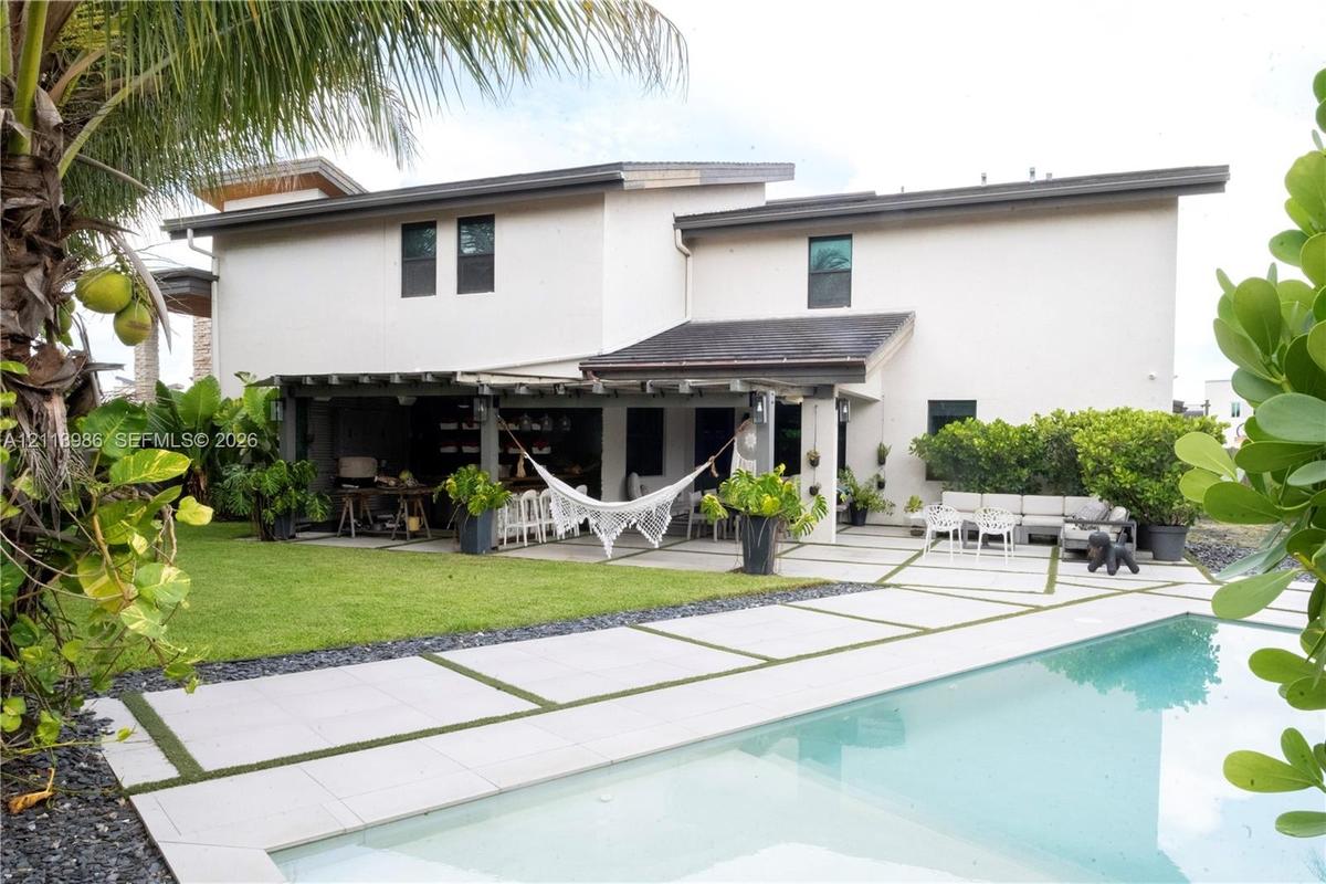 Rear exterior featuring a swimming pool with custom concrete paver hardscaping, integrated grass detailing, covered patio, and manicured lawn