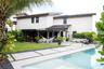 Rear exterior featuring a swimming pool with custom concrete paver hardscaping, integrated grass detailing, covered patio, and manicured lawn