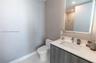 Modern vanity featuring a charcoal-finish cabinet, rectangular basin, and stone-surface countertop, complemented by a large integrated backlit mirror 