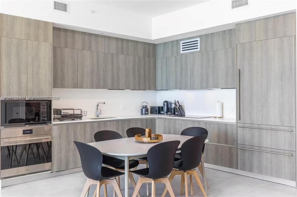 Kitchen featuring flat-panel wood-finish cabinetry, integrated refrigerator, built-in stainless steel microwave and wall oven, and light-toned solid s