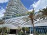High-rise architectural exterior featuring tiered glass balconies, metallic geometric facade paneling, floor-to-ceiling glass windows, and mature palm
