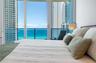 Floor-to-ceiling glass paneling featuring ocean and high-rise cityscape backdrops, with access to a private balcony enclosed by glass and metal railin