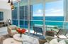 Floor-to-ceiling glass walls, expansive balcony with glass railings, built-in media shelving, and trio of pendant light fixtures