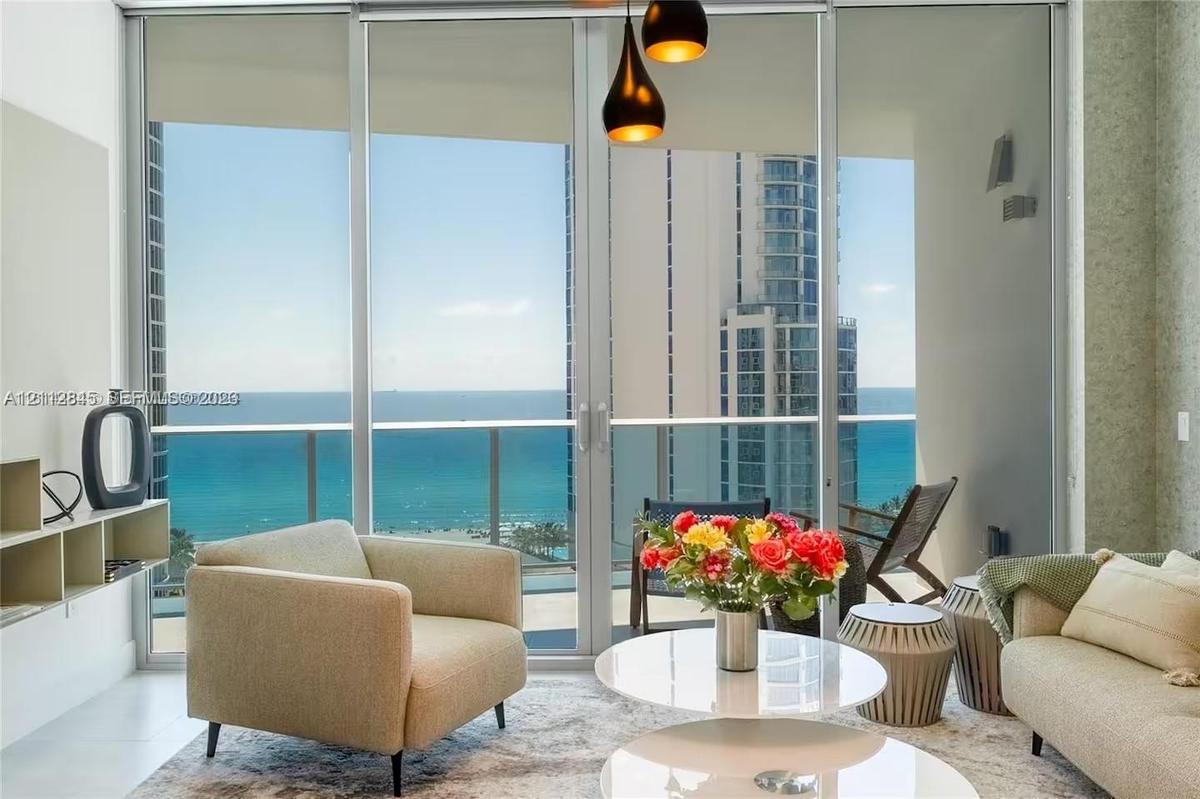 Floor-to-ceiling glass sliding doors, private balcony with metal railing, pendant light fixture with tiered shades, and custom built-in shelving