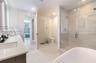 Bathroom featuring a dual-sink vanity with light-colored countertops, a freestanding soaking tub, and a glass-enclosed shower with tiled surround