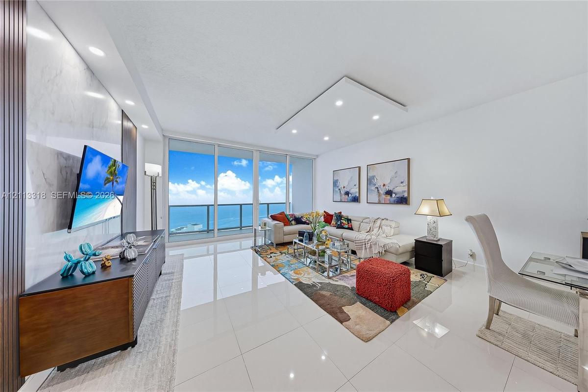 Living area featuring floor-to-ceiling glass sliding doors, polished tile flooring, recessed ceiling lighting, and a floor-to-ceiling stone-finish acc