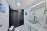 Walk-in shower with dark tile surround and glass enclosure, glass vessel sink, white vanity, and multi-bulb wall-mounted lighting